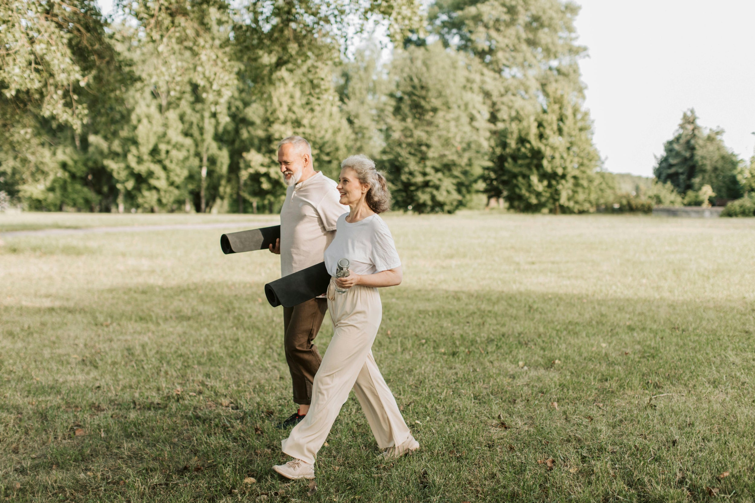 Two elderly people walking in a park with green grass and trees.